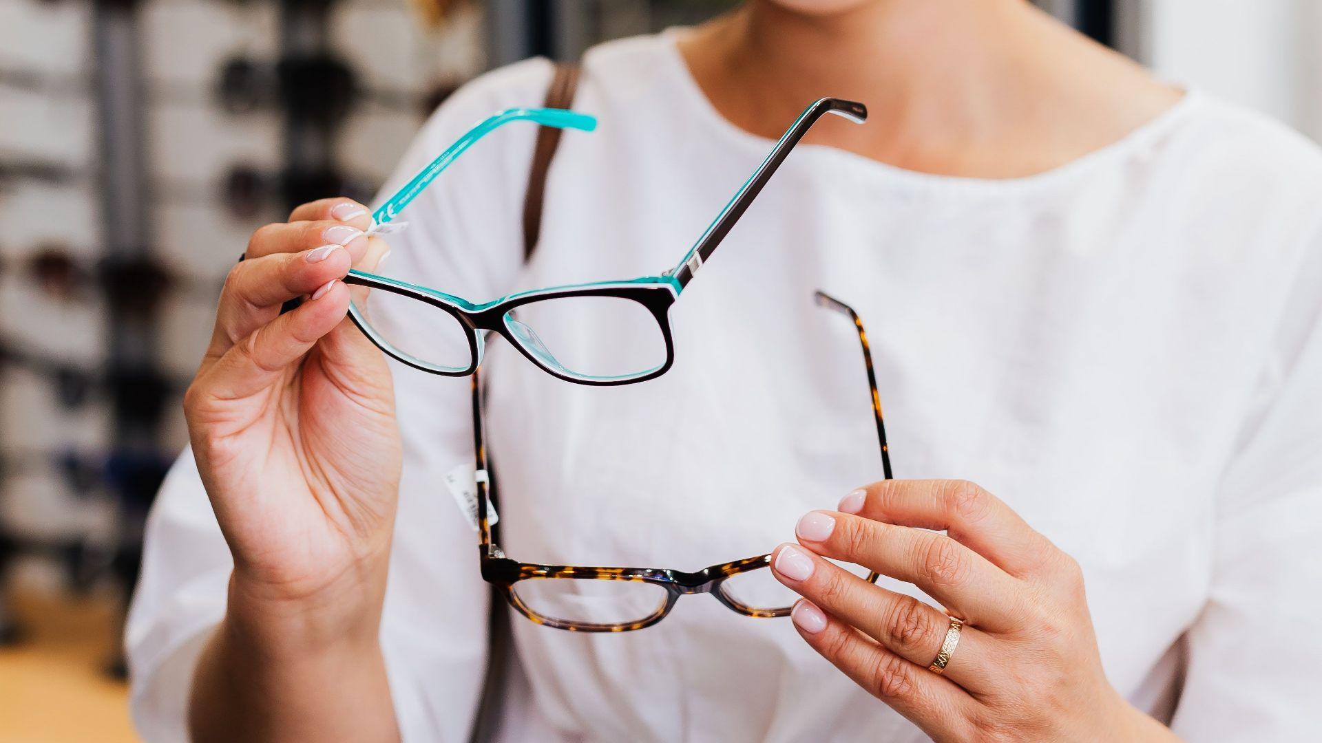 A woman examining eyeglasses options in an optical store, wearing a white dress.