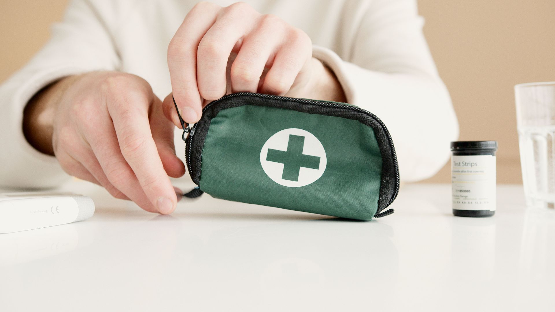 Close-up image of hands holding a first aid pouch on a table, with medical test strips nearby.