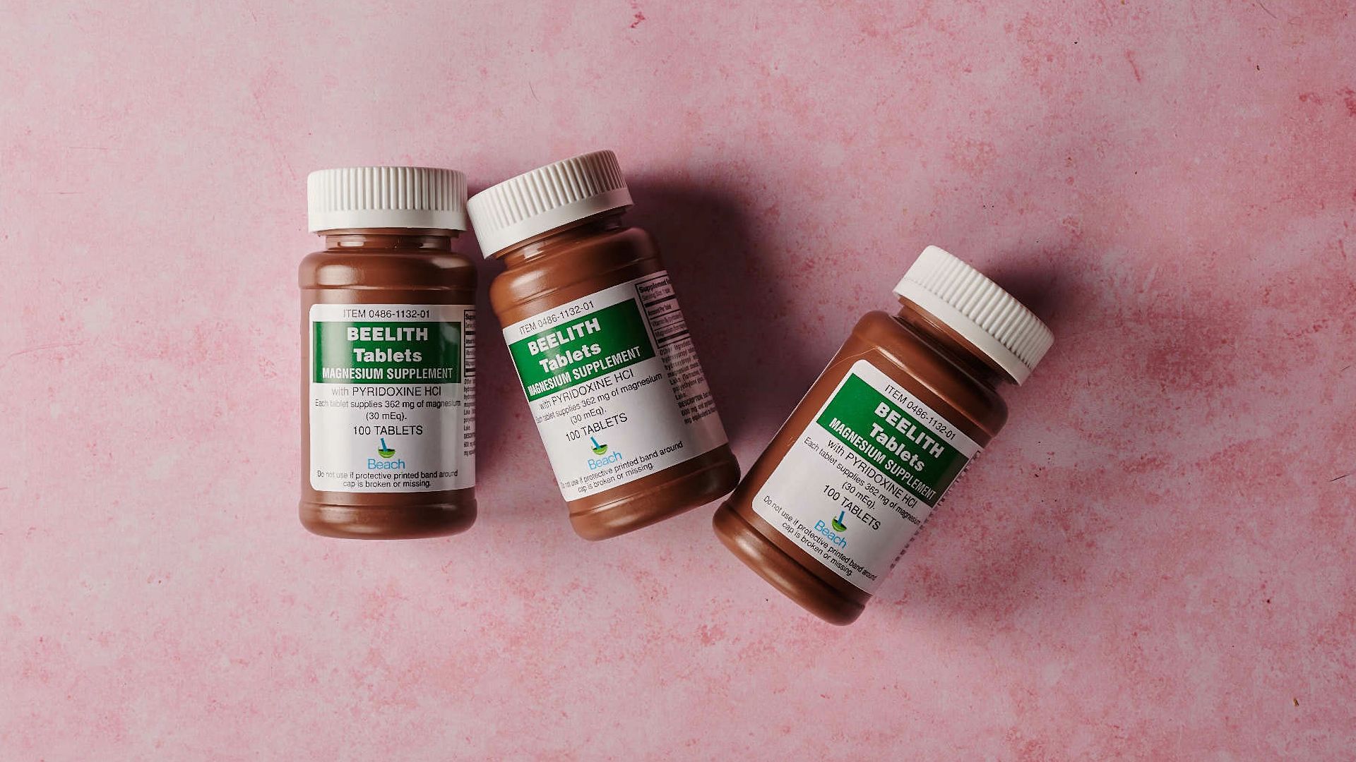 Three brown bottles of magnesium tablets on a soft pink background, ideal for health-themed content.