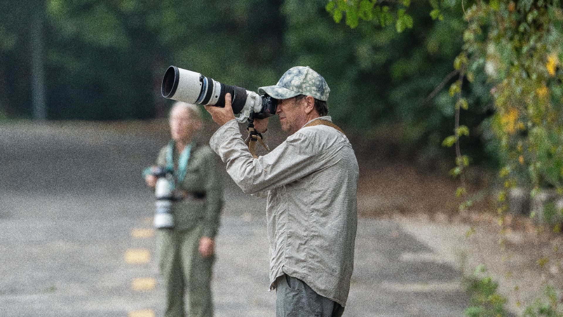 Two wildlife photographers capturing nature scenes with telephoto lenses, standing on a path.