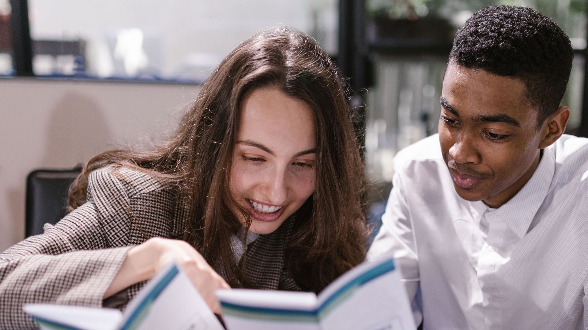 Two colleagues, a woman and a man, engaging in reading at an office setting.