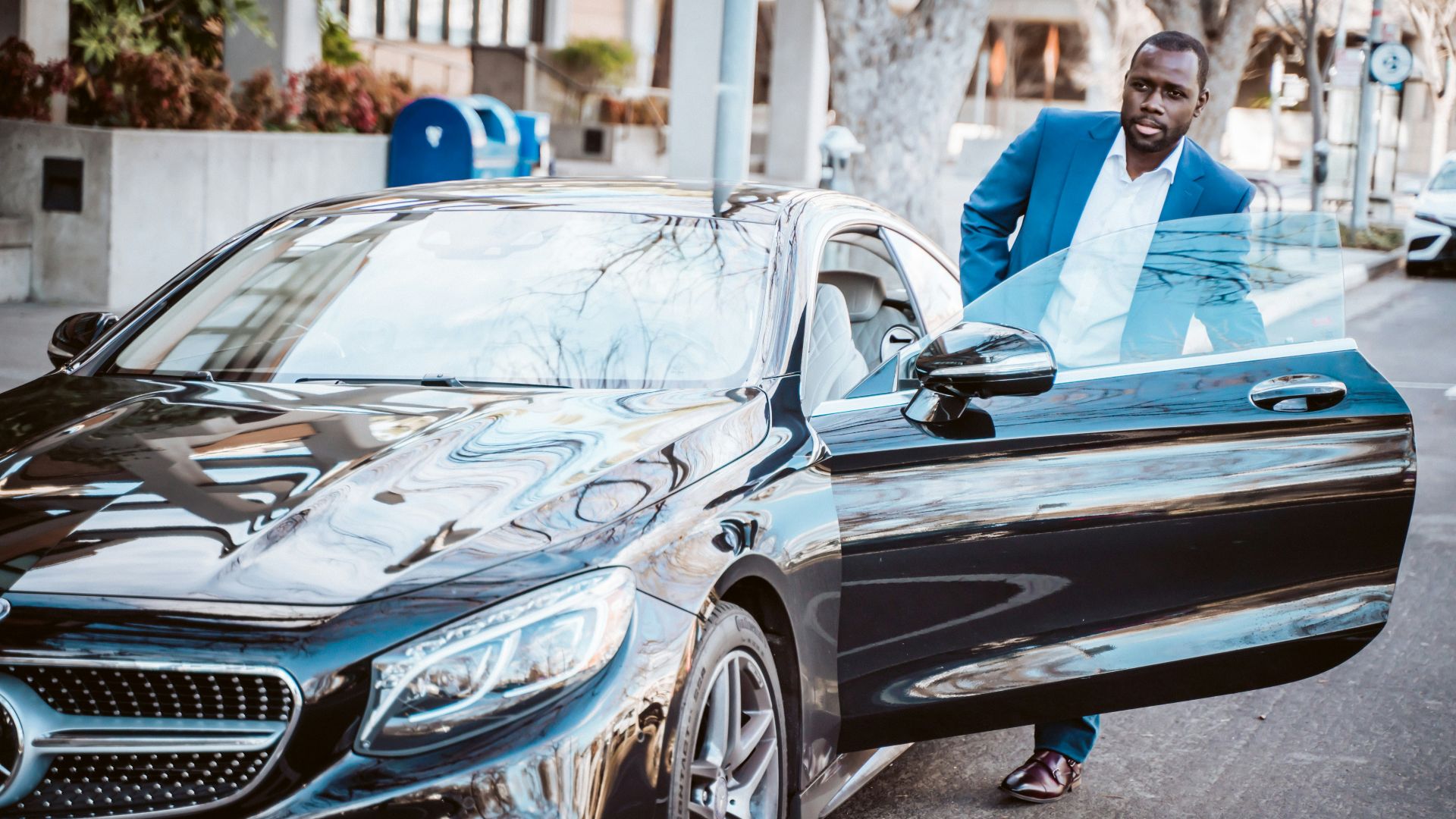 man in blue suit standing beside black car