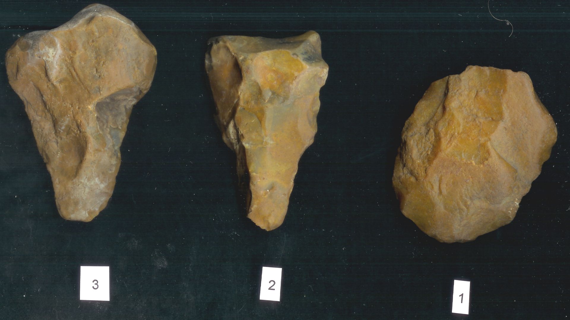 Lithic implements. 
    1. Acheulian hand axe: Flaking scars on both the ventral and dorsal sides around the edge, the tool is triangular in plan with a central point at the bottom, the butt is flat. The flaking scars are large a crude and flint has been 
