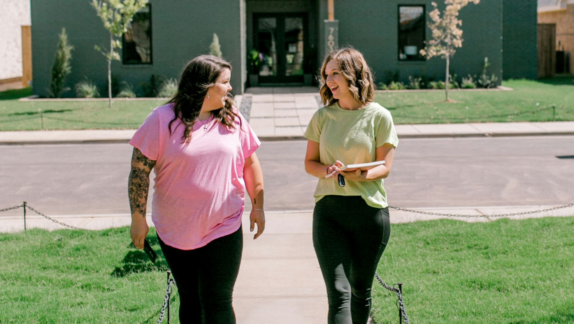 Two women converse while walking past a modern house.