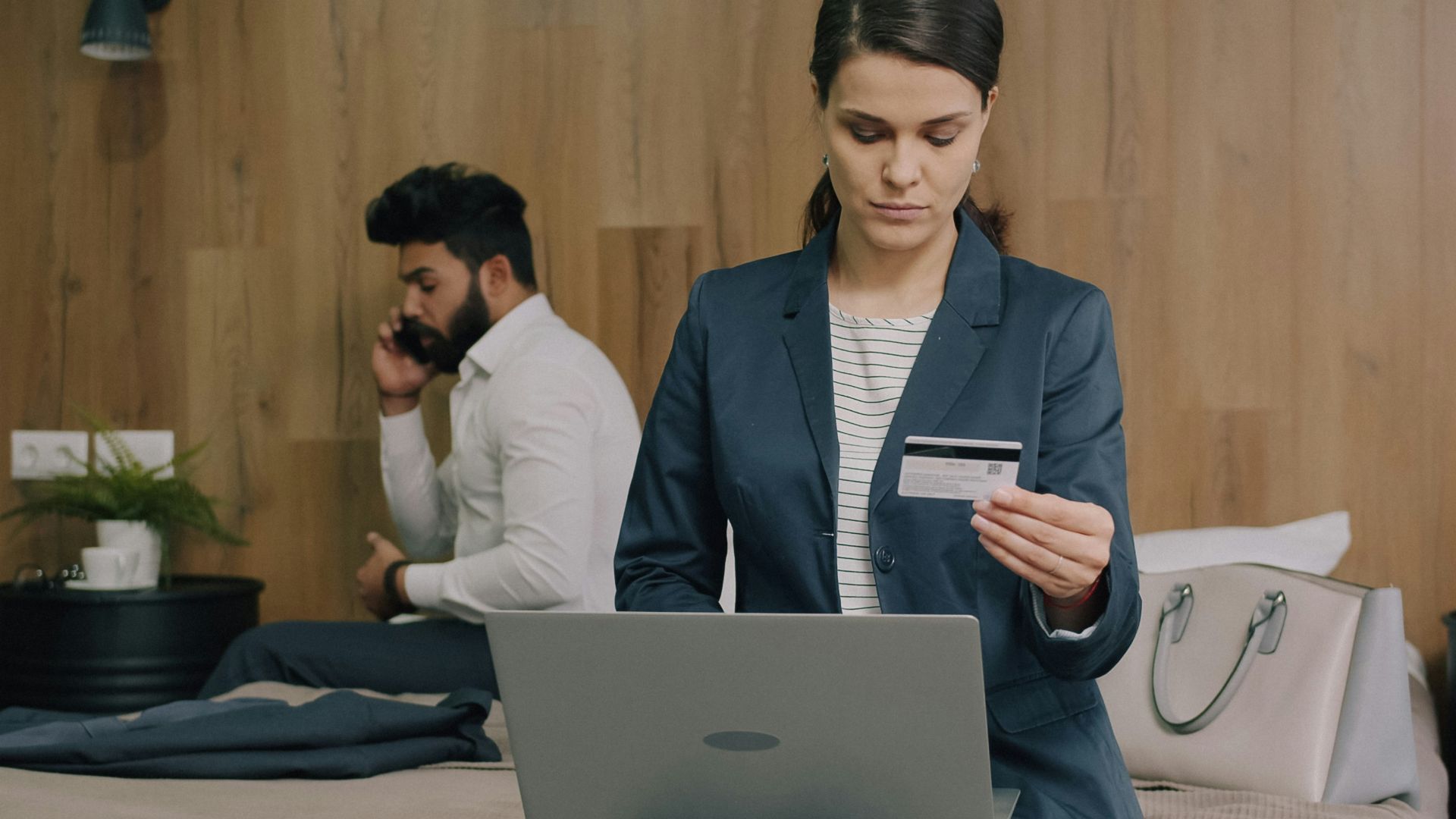 A woman in a blazer holding a credit card while using a laptop