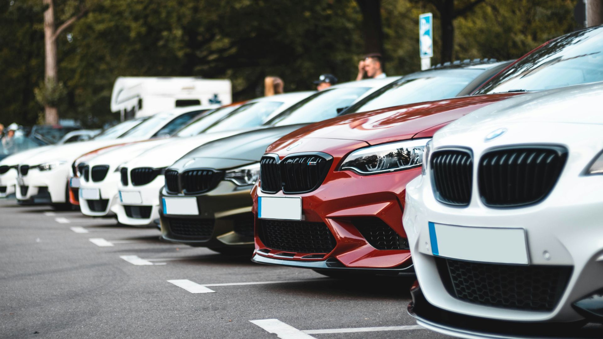 A row of parked cars including white, olive, and red sedans in a lot