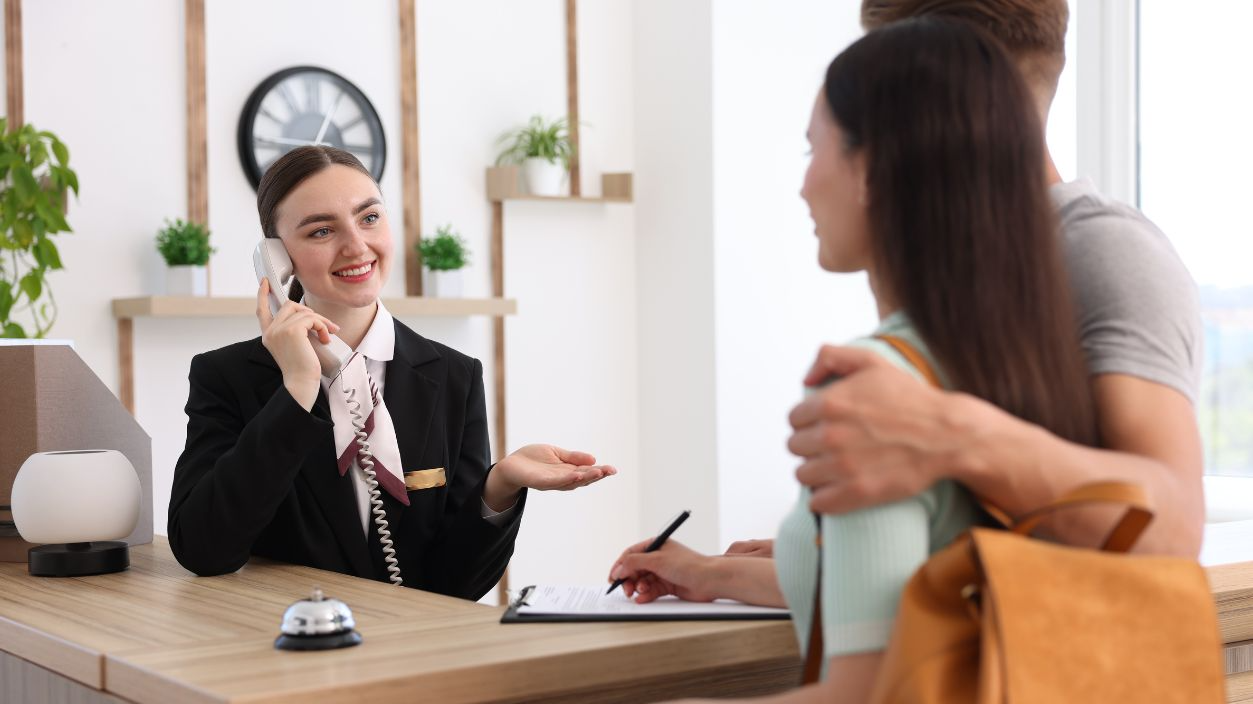 Shutterstock-2663003275, Smiling receptionist working with clients at reception desk in hotel