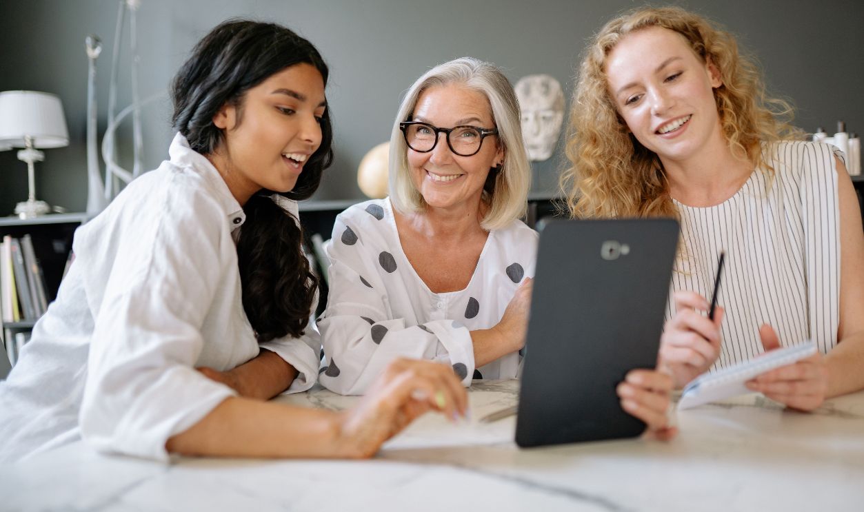 Three diverse women collaborate in a modern office setting, fostering teamwork and innovation