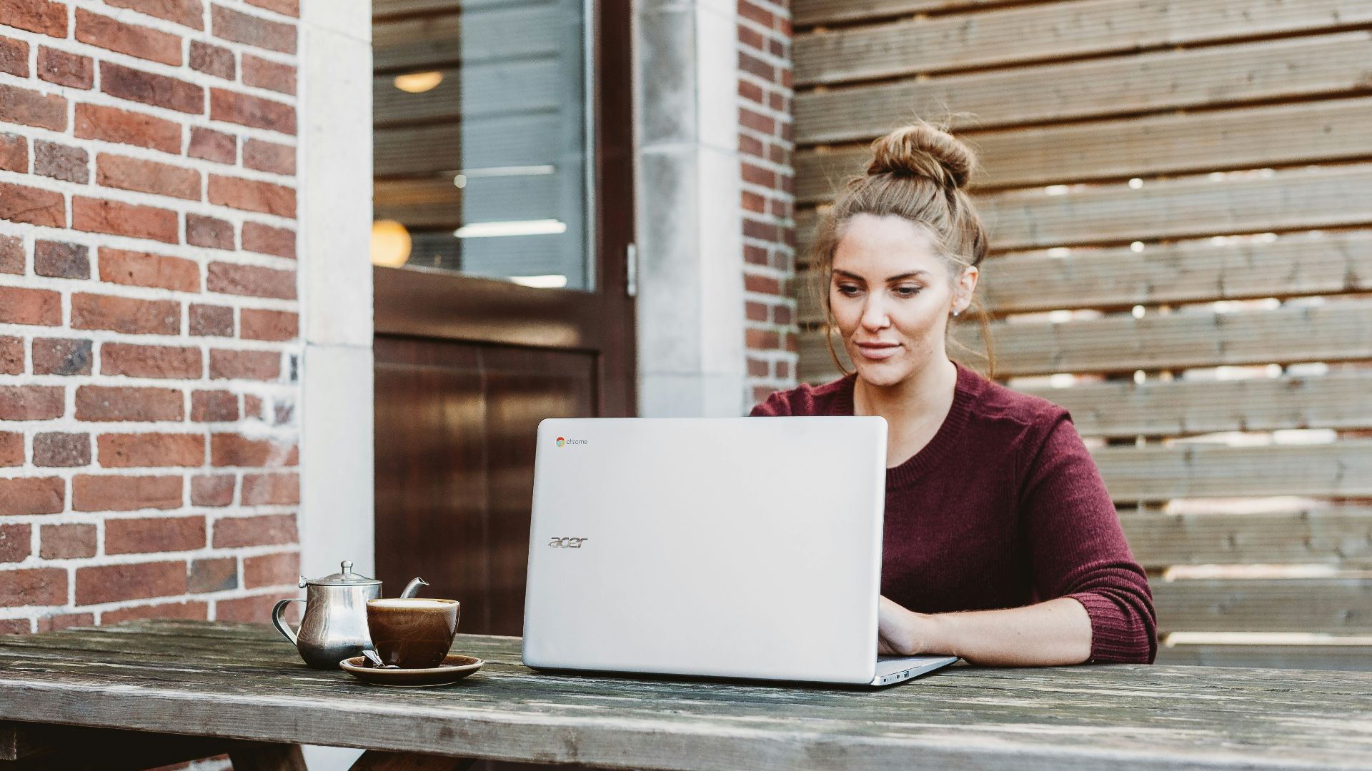 woman sitting and holding white Acer laptop near brown wooden wall