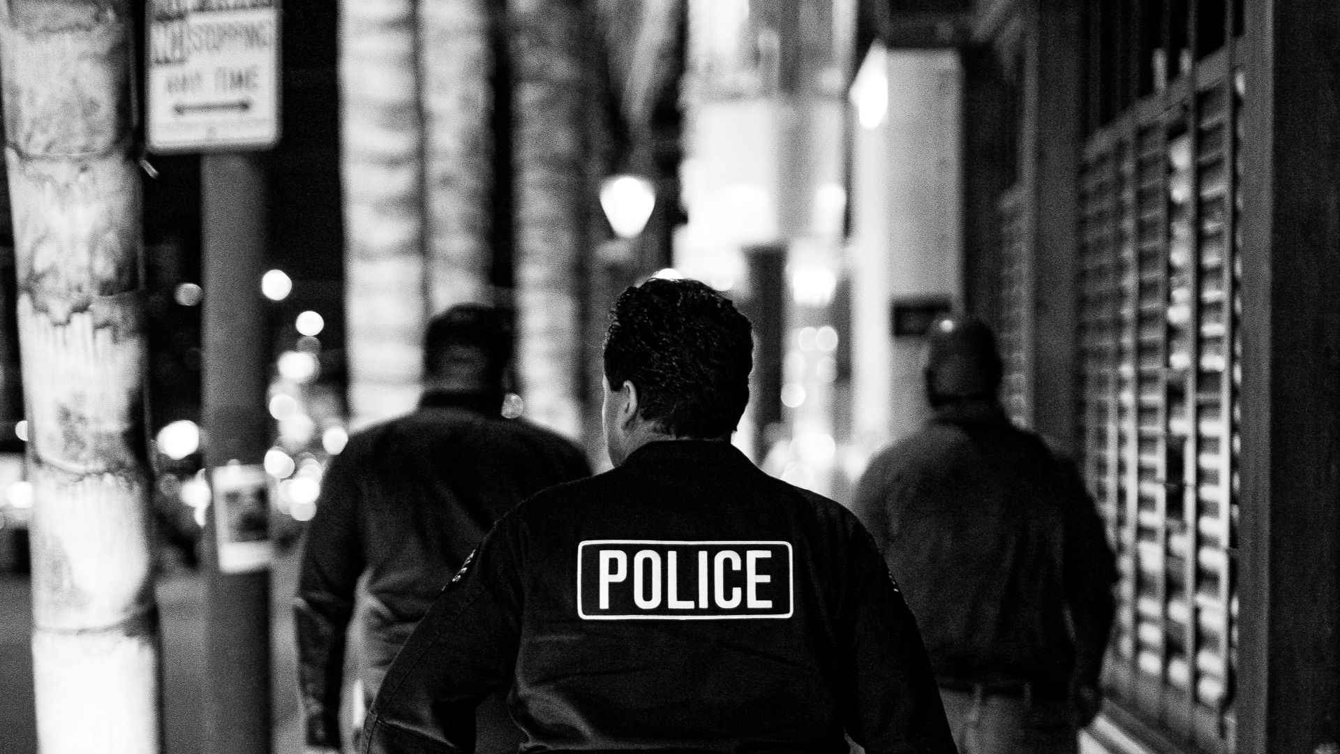 grayscale photo of man in black jacket and pants walking on sidewalk