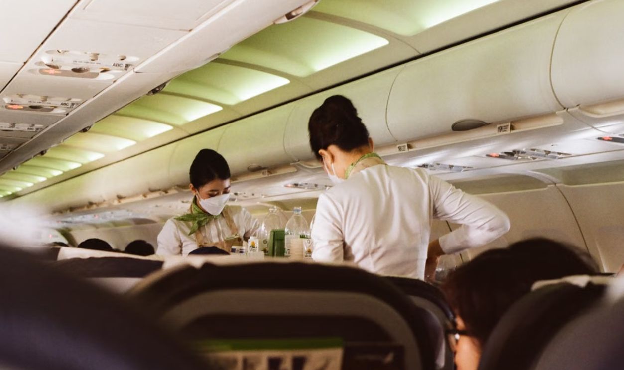 Flight attendants in white uniforms and masks serving passengers onboard a Vietnam airplane.