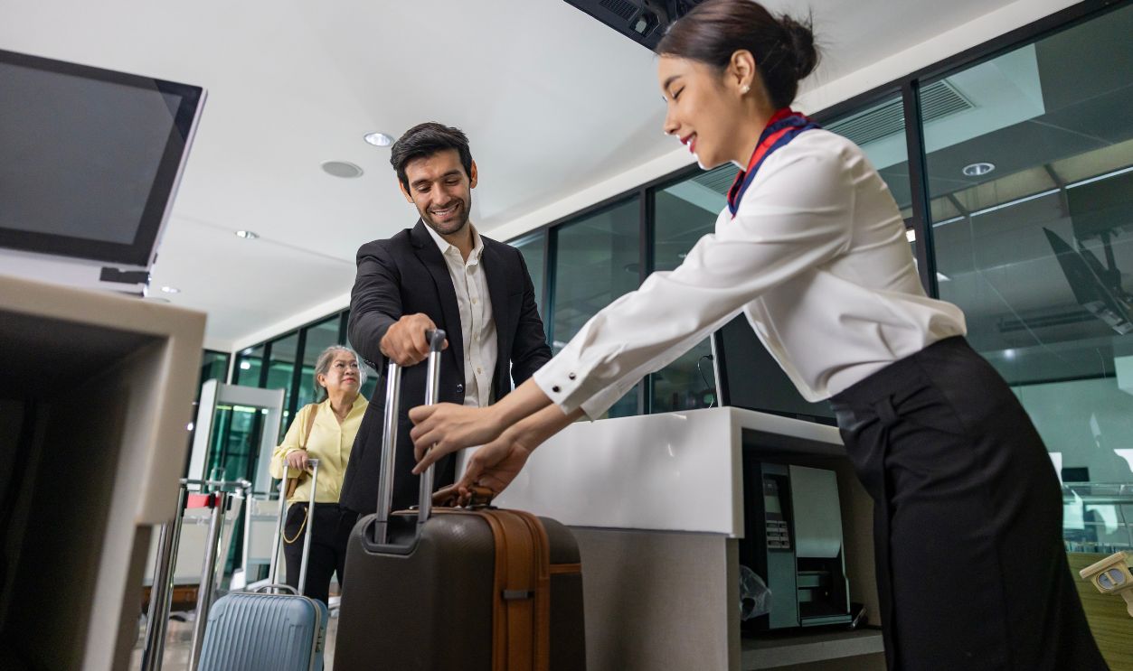 Caucasian businessman passenger is checking in big baggage bag to airline ground crew at departure gate into the airplane for measuring weight before boarding plane