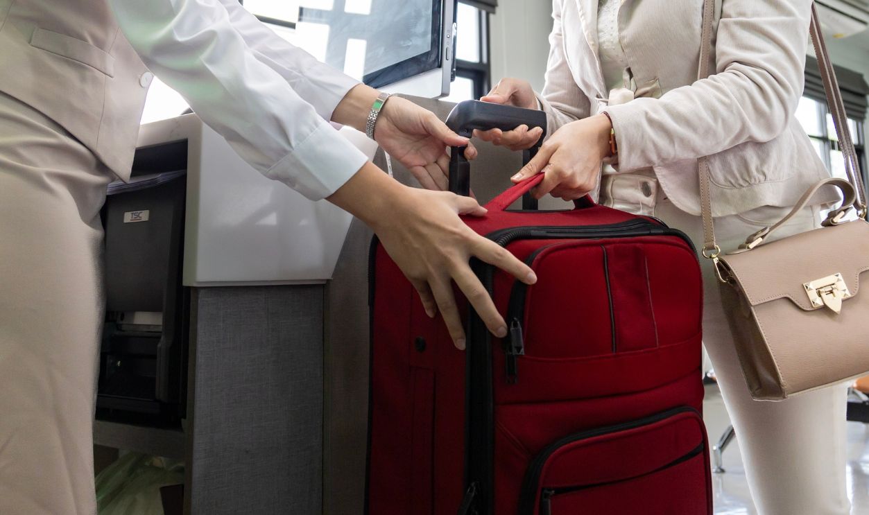 Asian passenger is checking in her big baggage bag to airline ground crew at departure gate into the airplane for measuring weight before boarding into plane