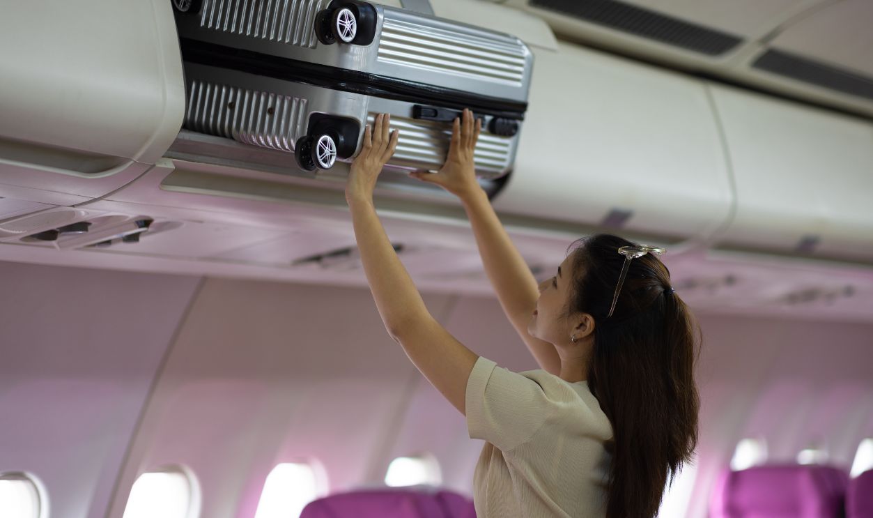 Female tourist packing her luggage in the airplane cabin.