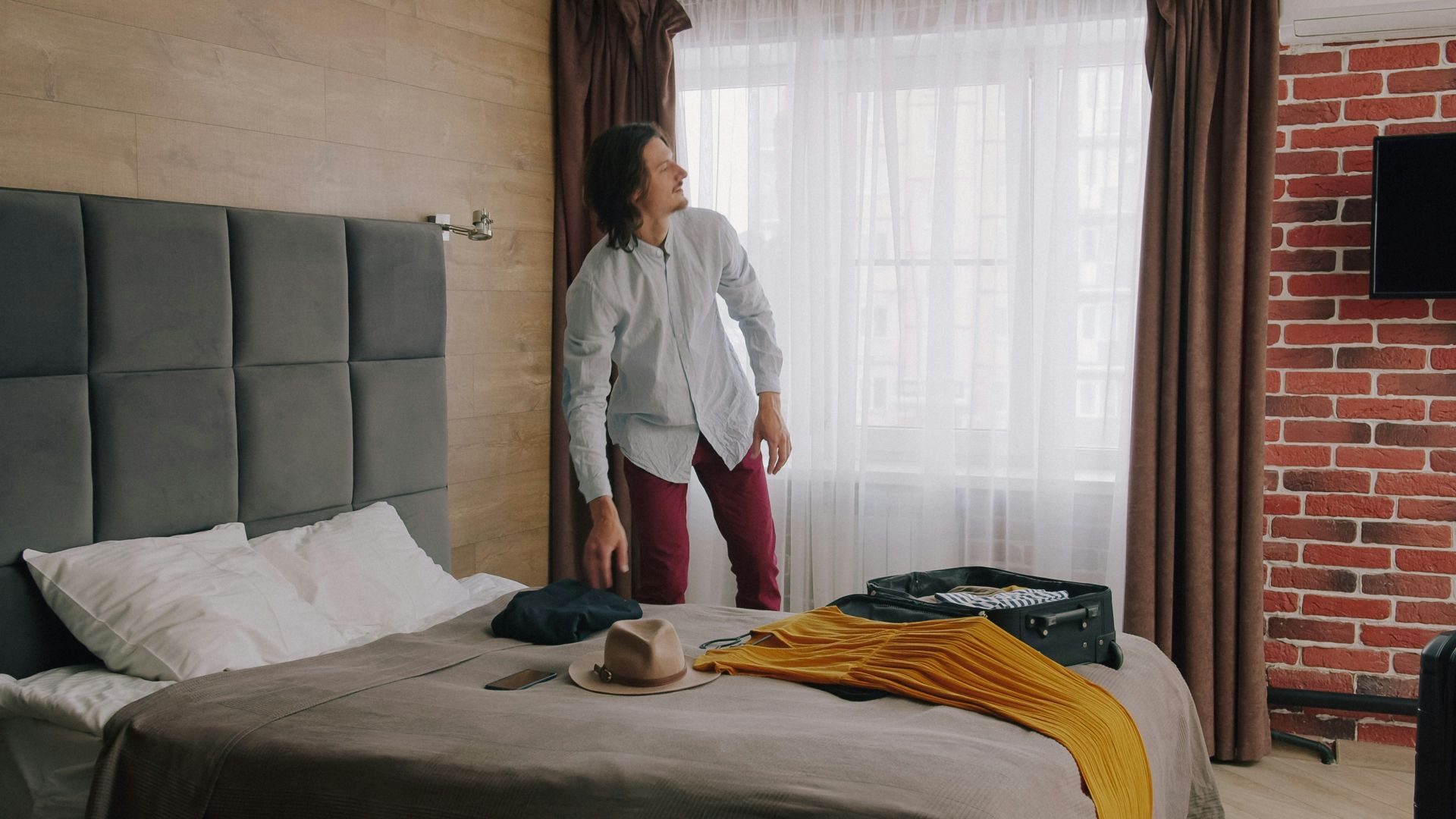 A man in a light shirt and red trousers packing a suitcase on a bed