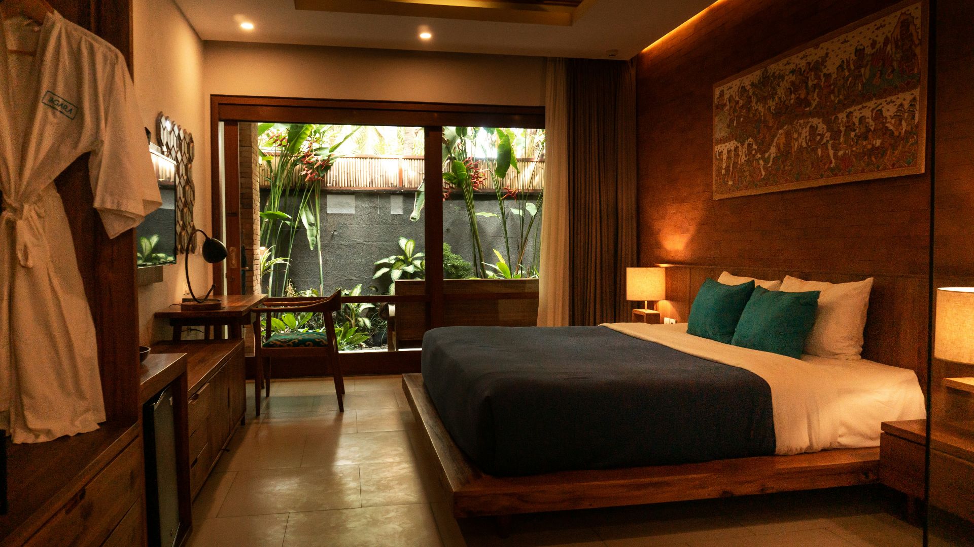 A hotel bedroom with a wooden bed, teal pillows, and a private garden view