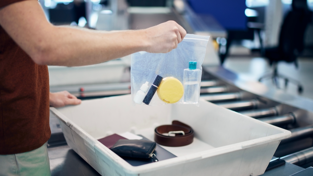 Passenger holding plastic bag with liquids above container personal items