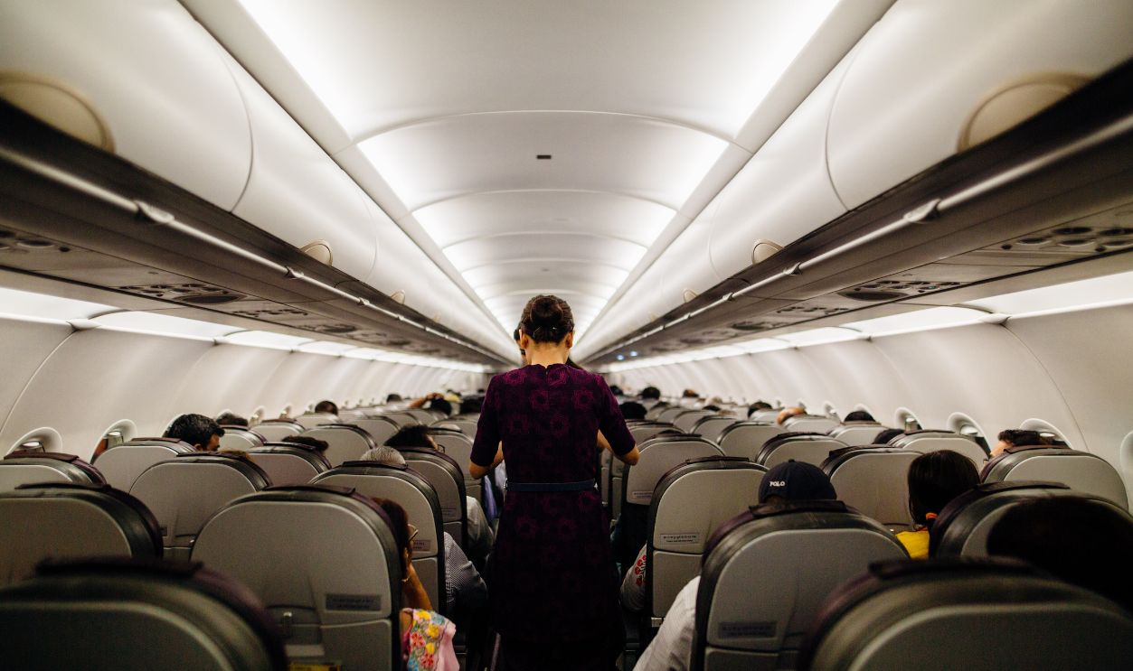 Interior view of an airplane cabin with passengers seated and a flight attendant walking down the aisle