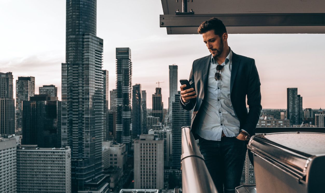 Man in black suit using phone on a Toronto rooftop with skyline view