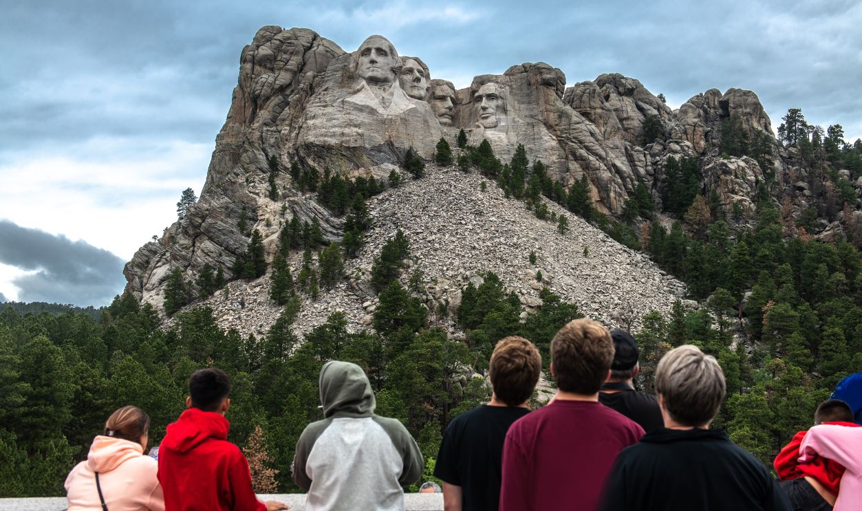 Tourists taking pictures and observe mountain Rushmor with USA presidents sculptures.