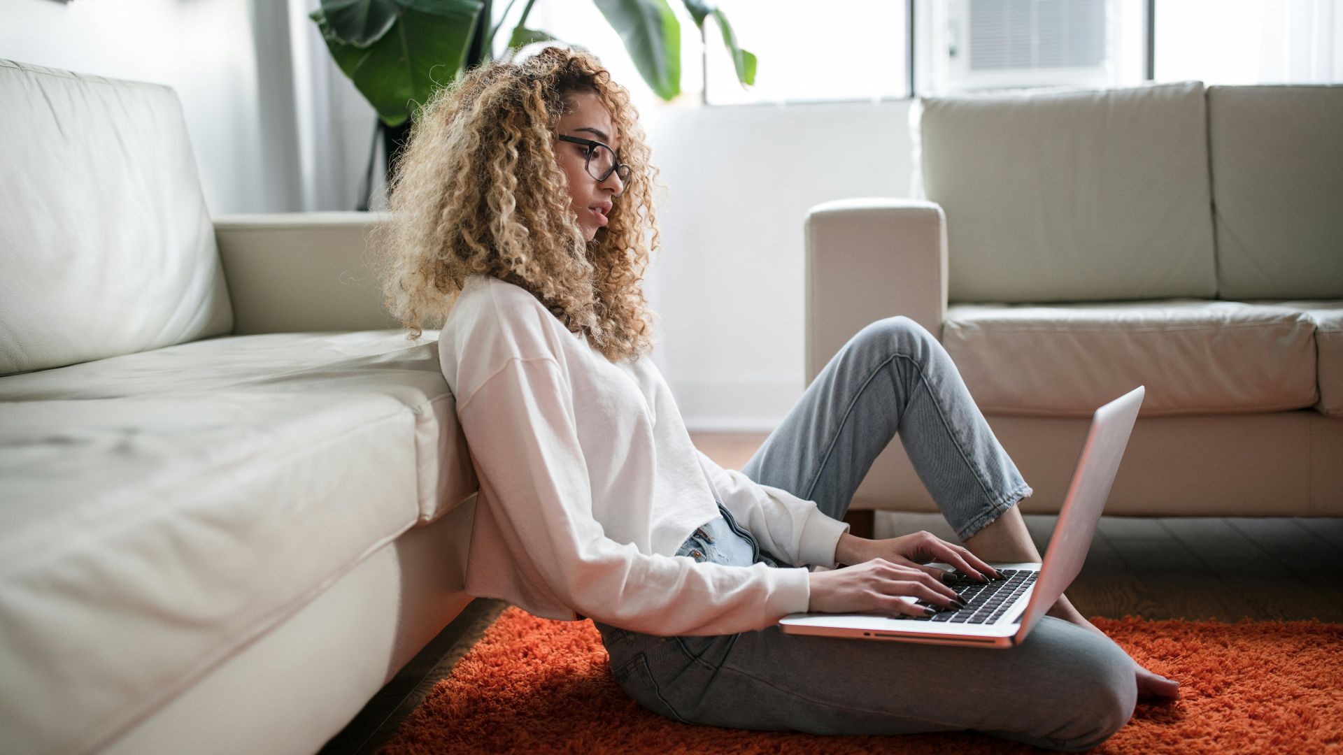 woman sitting on floor and leaning on couch using laptop