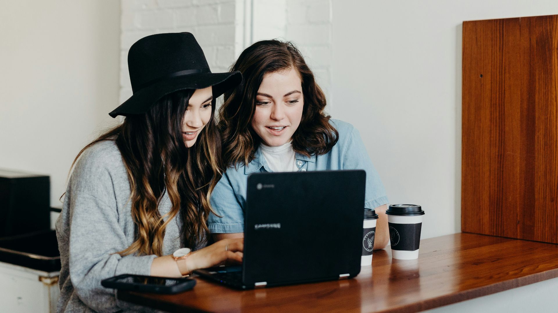 two woman sitting near table using Samsung laptop