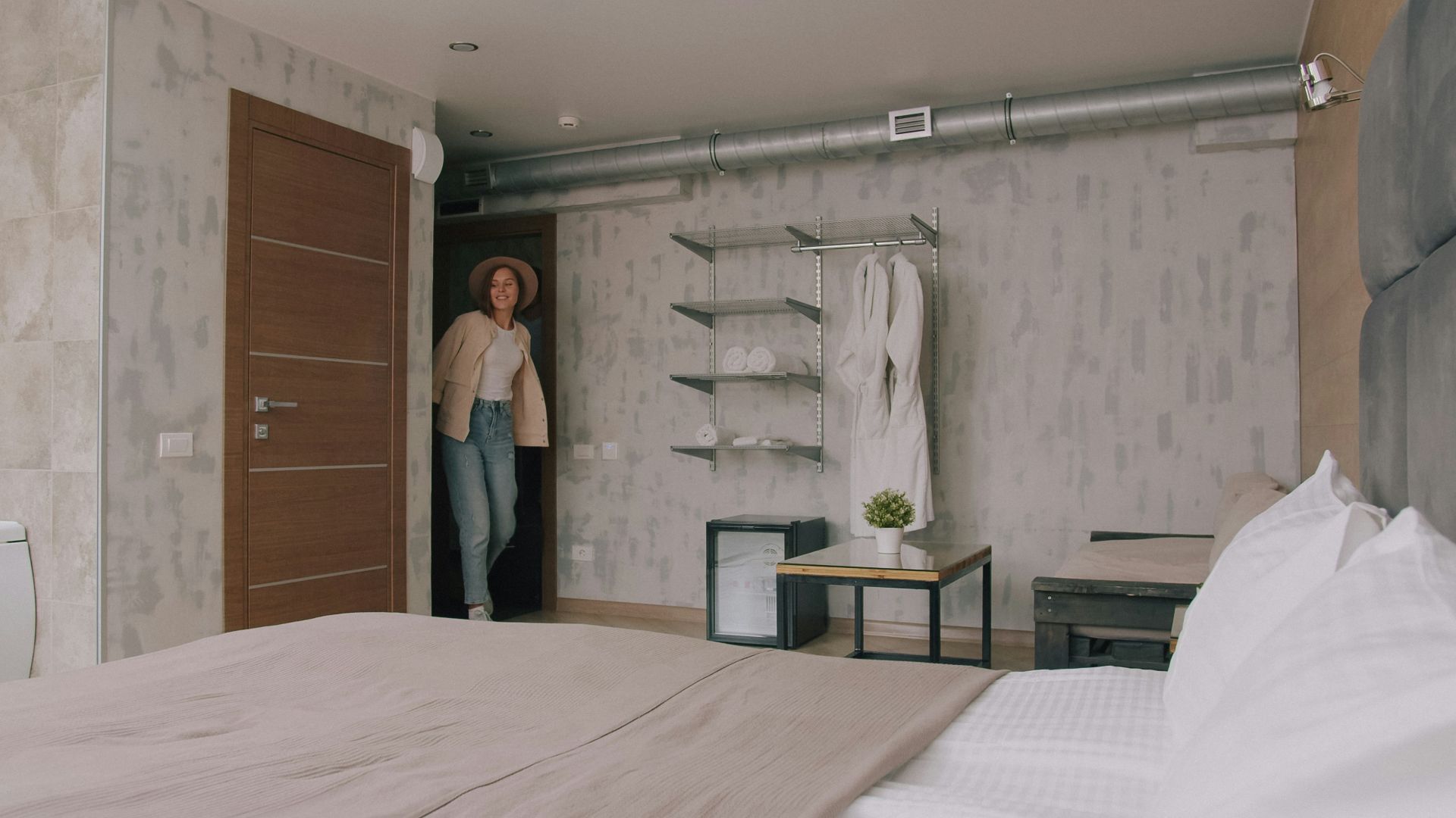 A woman in a hat and jacket entering a modern hotel room
