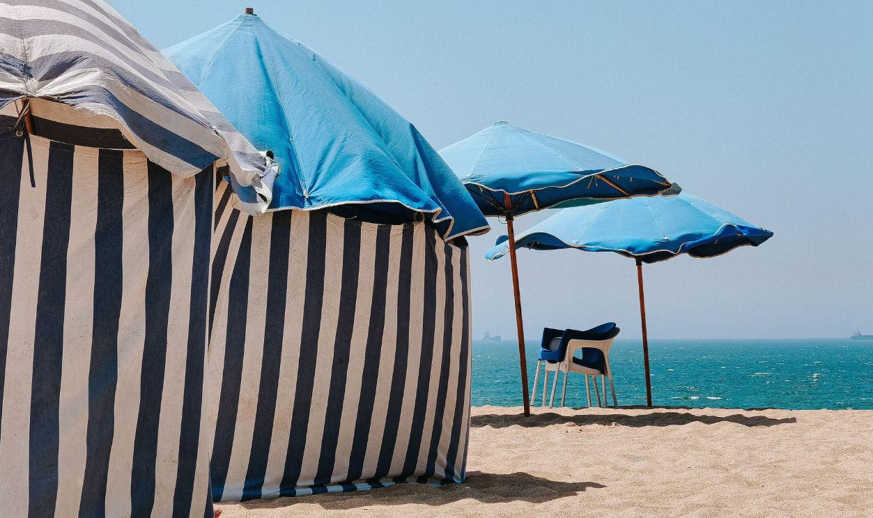 Striped tents and blue umbrellas on the sandy beach of Figueira da Foz, Portugal, with a serene ocean