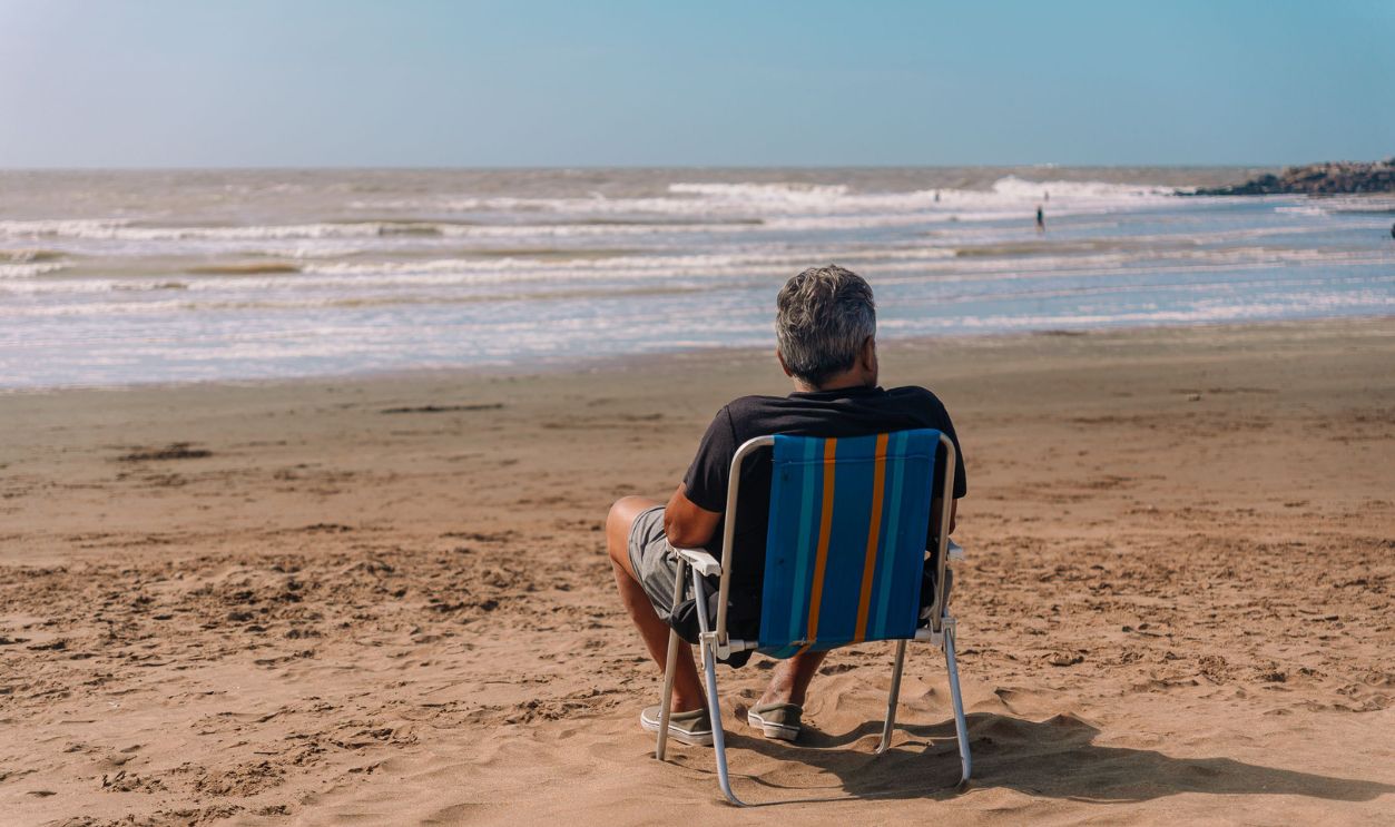 An adult man relaxing on a colorful chair by the ocean on a sunny day, enjoying the peaceful beach