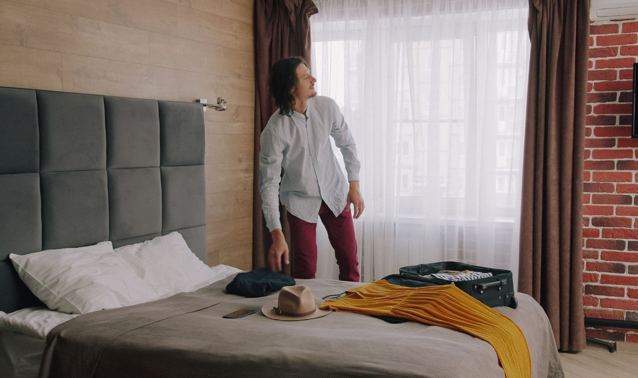 A man prepares for travel in a stylish hotel room, packing a suitcase on the bed
