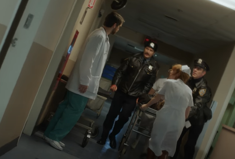 Screenshot of The Lennon Report (2016) showing police officers carrying John Lennon to hospital