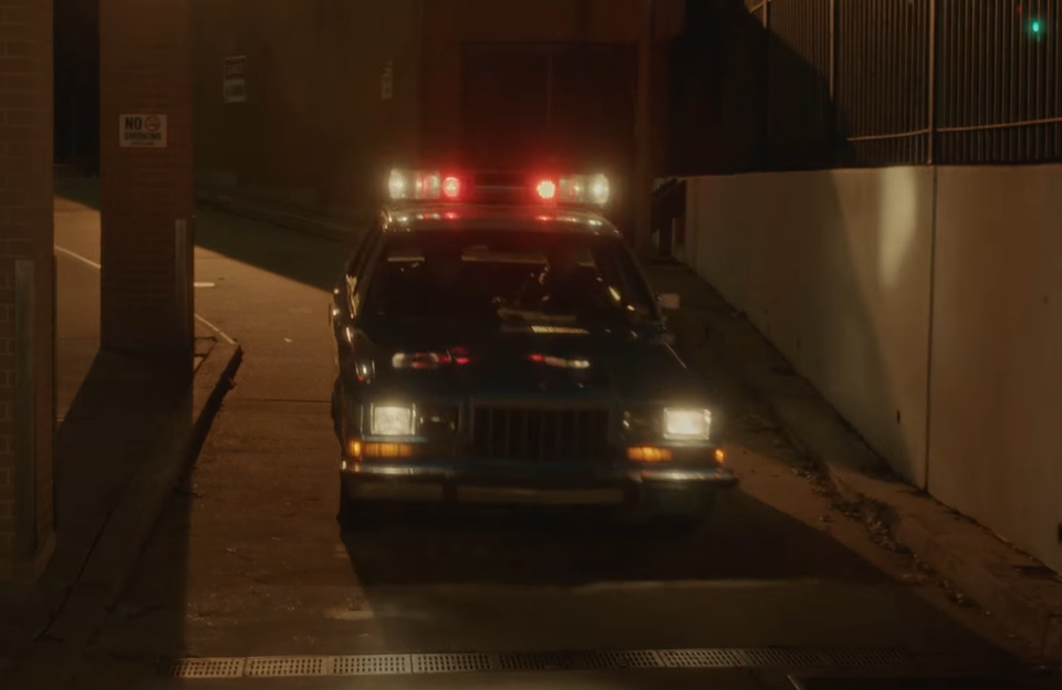 Screenshot of The Lennon Report (2016) showing police officers carrying John Lennon in their car