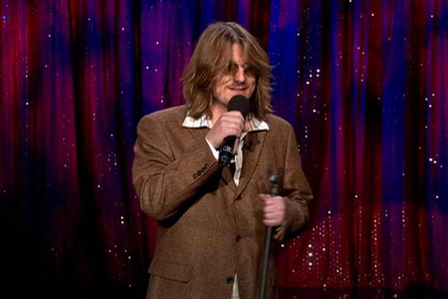 Mitch Hedberg  in brown suit  performing