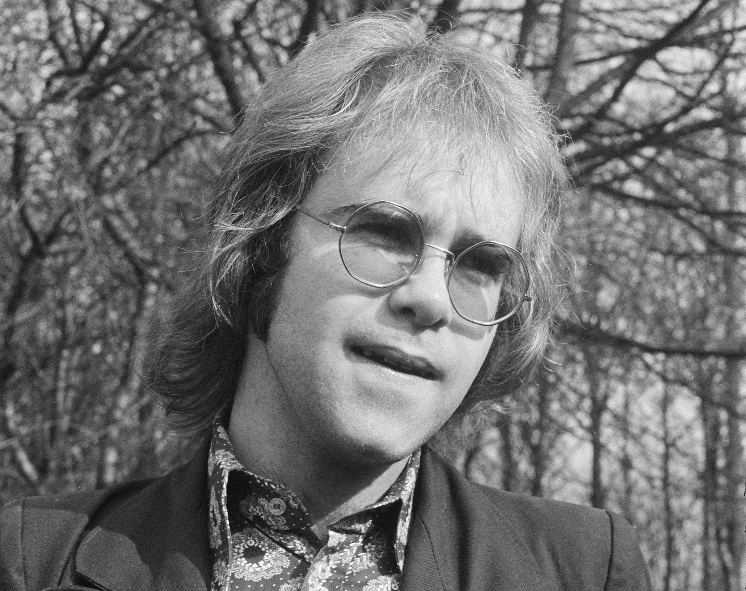 Grayscale Portrait Photo of Elton John wearing a jacket and floral shirt