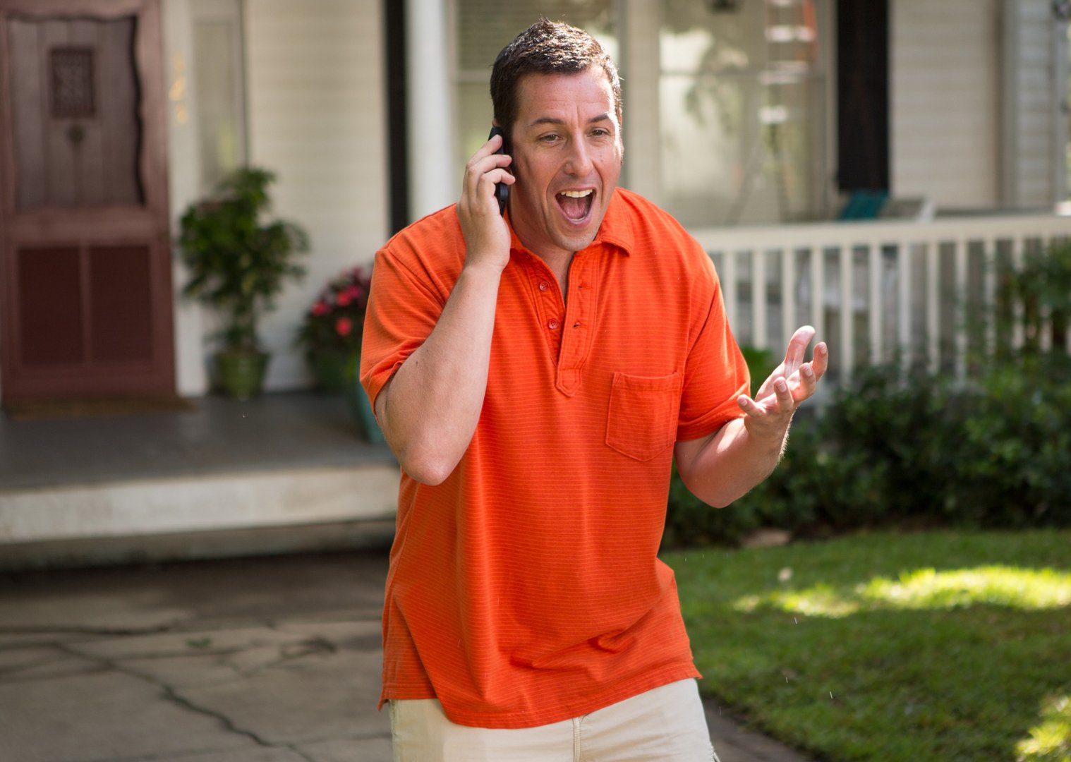 Portrait Photo of Adam Sandler in orange shirt speaking on the phone