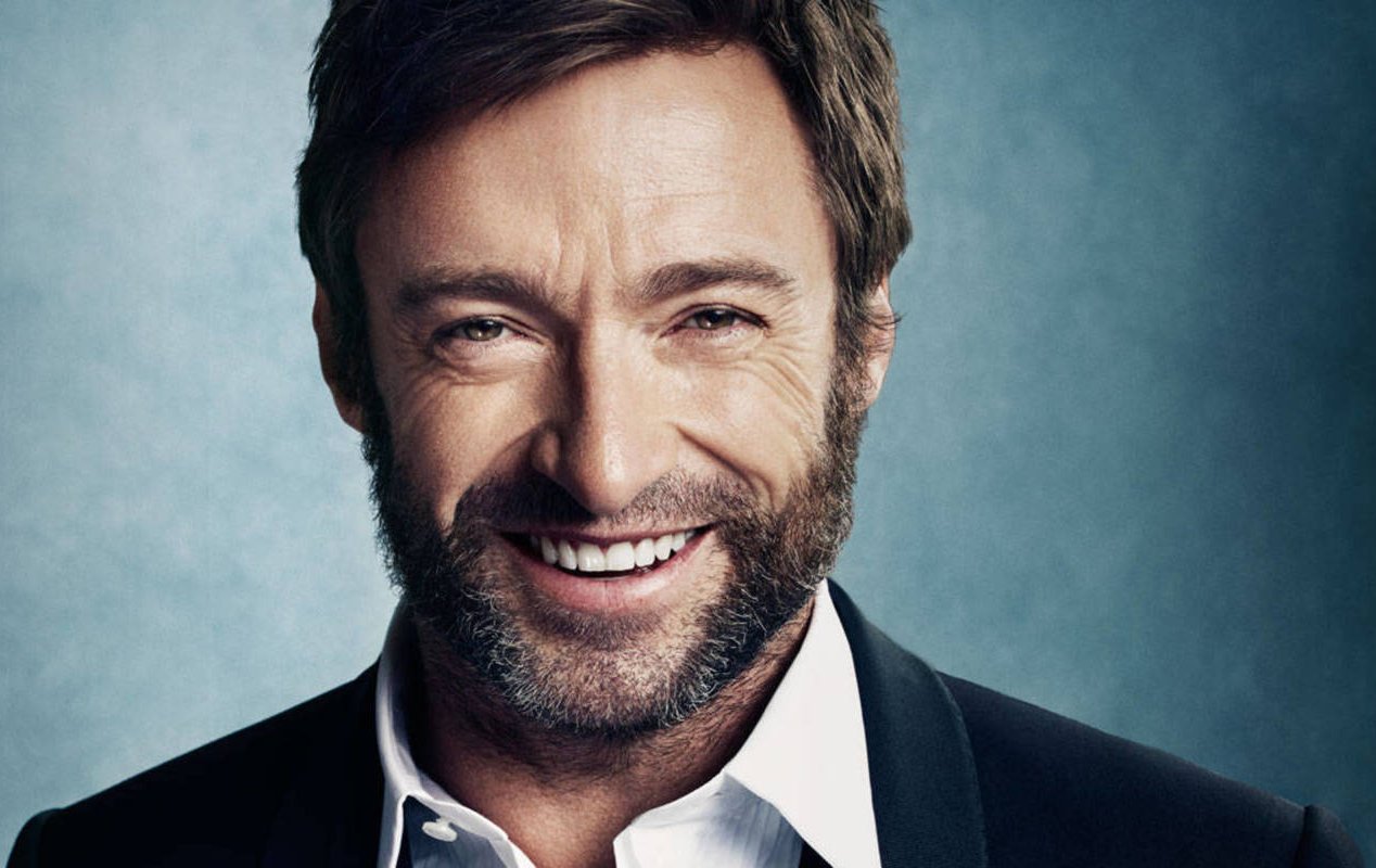 Portrait Photo of Hugh Jackman in a dark suit, smiling and facing the camera