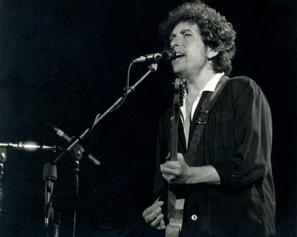 Grayscale Portrait Photo of Bob Dylan performing on stage with his guitar