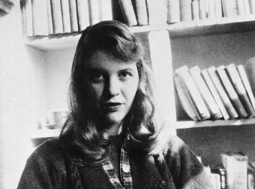 Sylvia Plath seated in front of a bookshelf