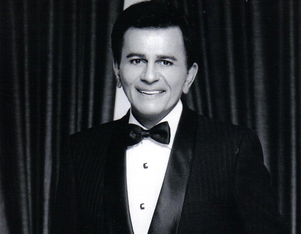 Grayscale Portrait Photo of Casey Kasem in a dark suit smiling and facing the camera.