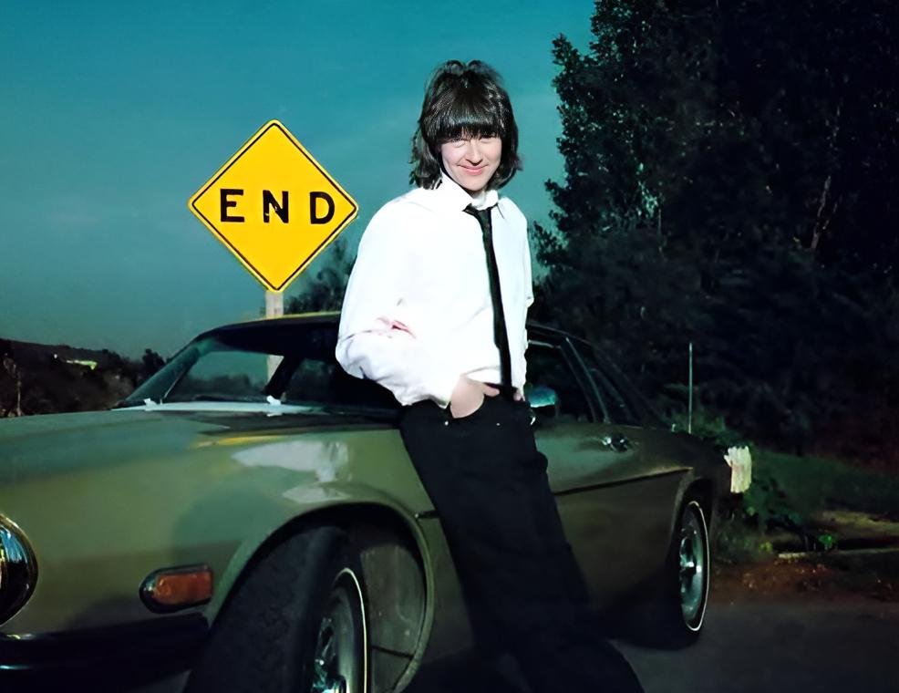 Portrait Photo of Randy Meisner in a white shirt leaning on a car