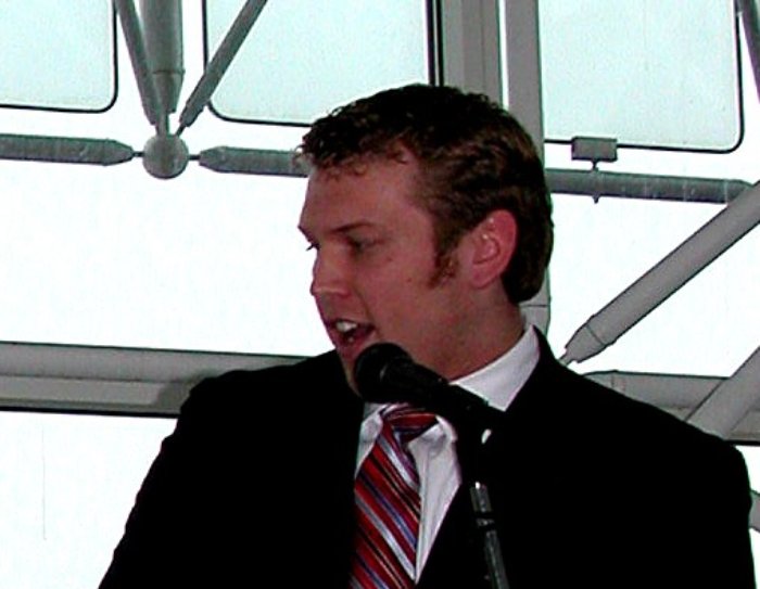 Chris Nowinski in a dark suit speaking in front of a microphone