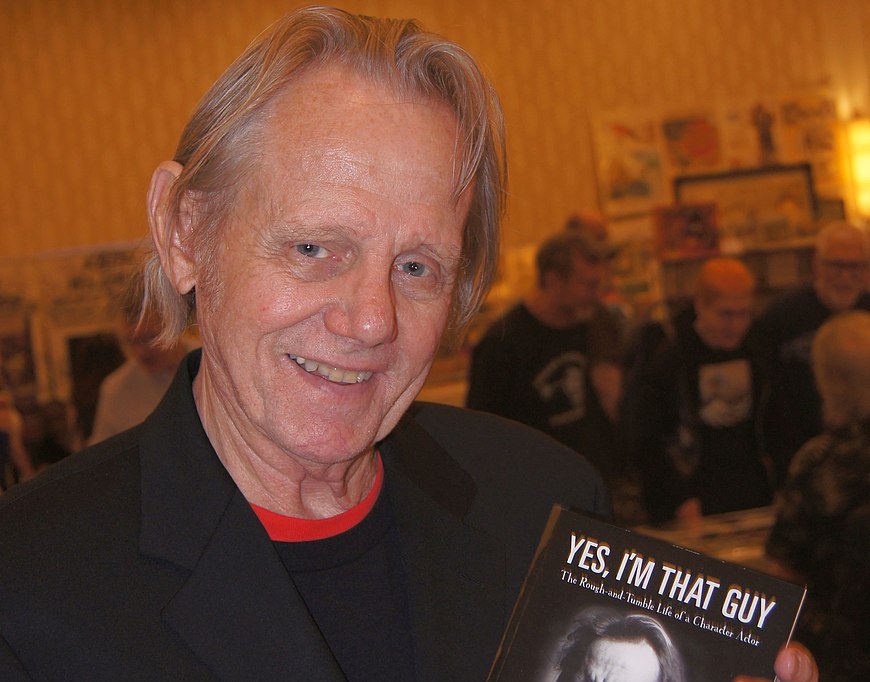 Portrait Photo of William Sandersen in a dark outfit, holding a book
