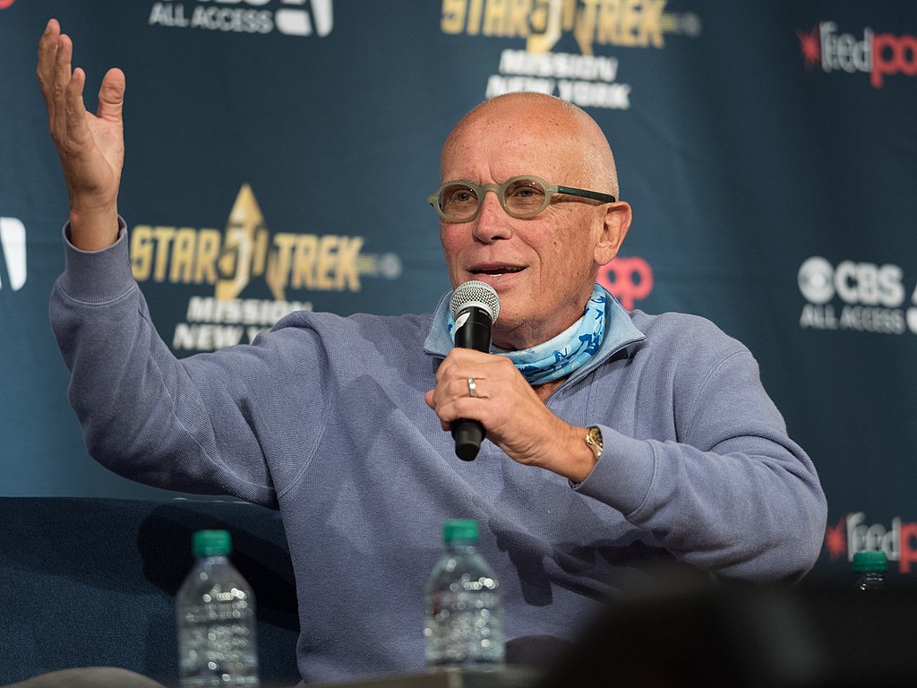 Portrait Photo of Peter Weller in a blue outfit, holding a microphone