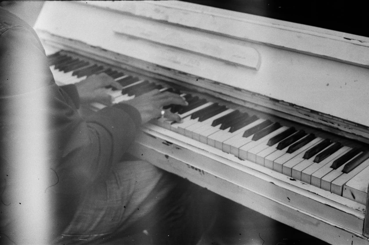 Grayscale Photo of a Person Playing on Vintage Piano