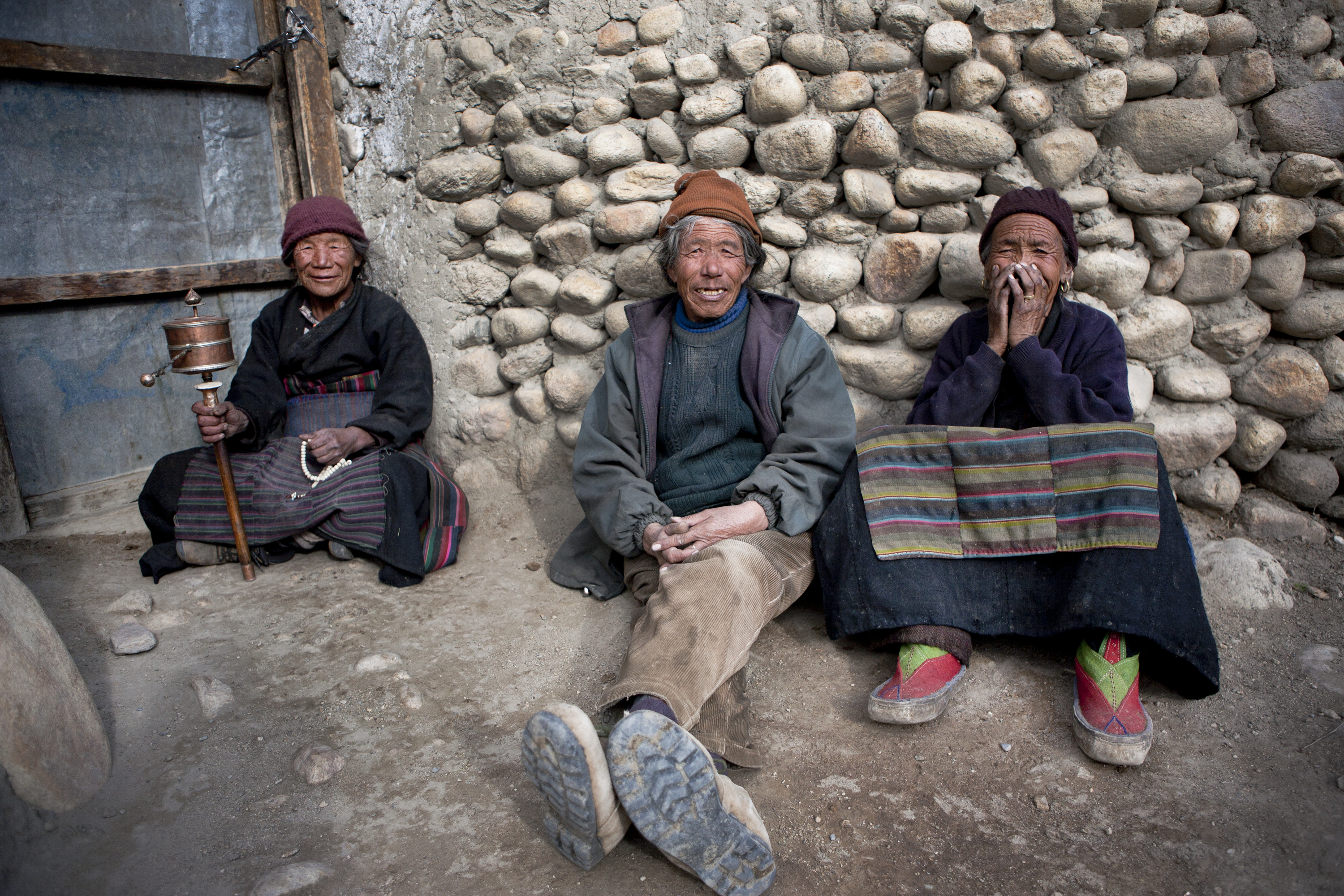 Elderly Loba gather in a patch of sunlight in Tsarang to spin prayer wheels and chat