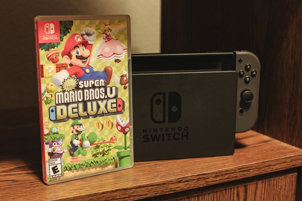 The video game Super Mario Bros U Deluxe, next to a Nintendo Switch, on a shelf.