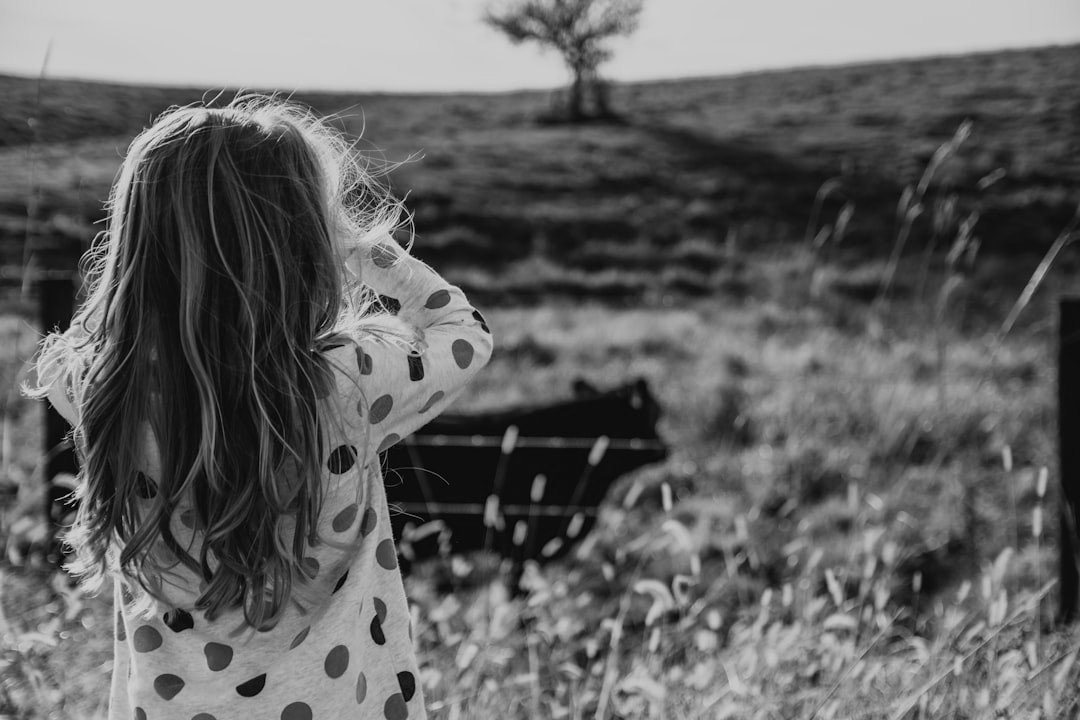 girl wearing white and multicolored polka-dot long-sleeved shirt standing while facing back on green field during daytime