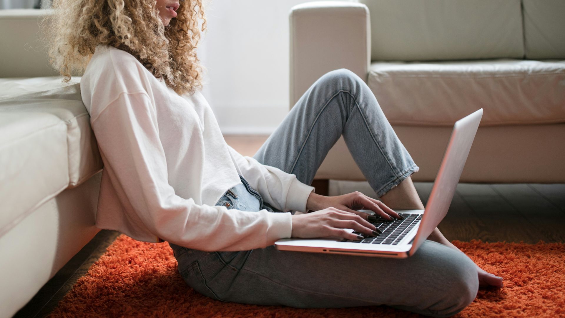 woman sitting on floor and leaning on couch using laptop