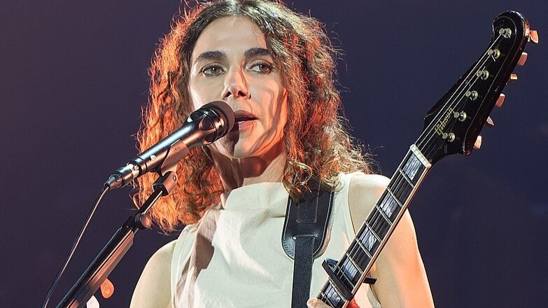 Portrait Photo of PJ Harvey in a white dress performing on stage