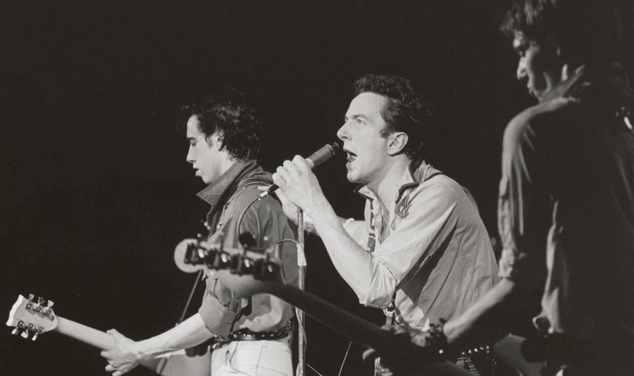 The Clash's Joe Strummer sings at a concert flanked by guitarists Mick Jones and Paul Simonon. 